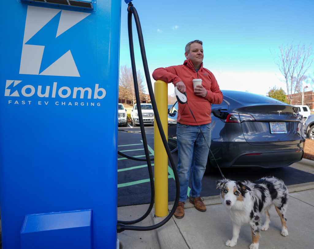 person standing with a dog next to a Koulomb EV charging station while charging their car